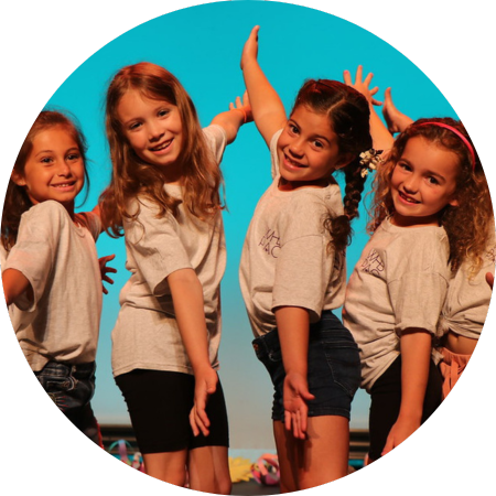 Smiling children stand in a line and do jazz hands in an aesthetically pleasing way on the WHBPAC.