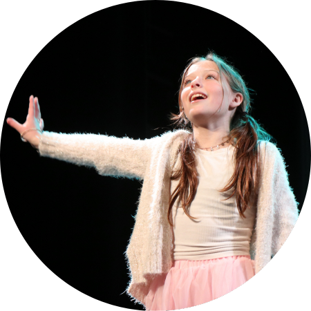 Lit up by stage lights, a girl in pigtails in front of a dark green background sings her heart out.