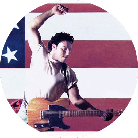 A Bruce Springsteen lookalike stands dramatically in front of the American flag, about to strike his guitar.