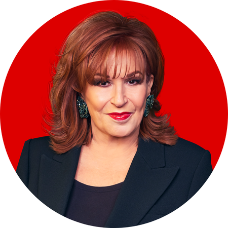 Joy Behar, a woman with styled auburn hair, poses confidently against a bright red background. She wears a black blazer over a black top, along with bold, sparkly green earrings. Her expression is poised and self-assured, with a subtle, knowing smile, creating a polished and charismatic presence.